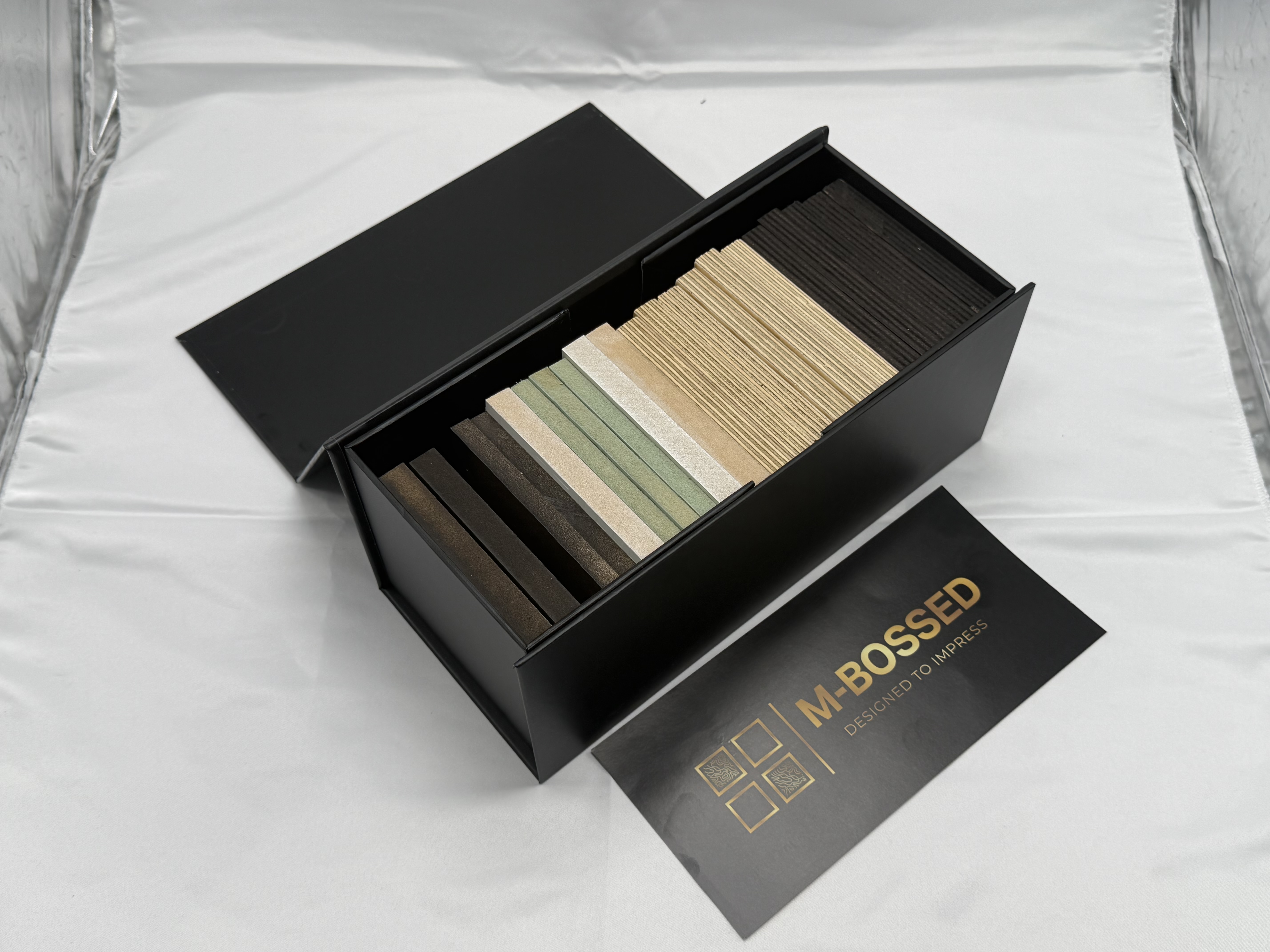 M-Bossed Sample Box opened, showing 21 coaster samples across all six signature patterns and finishes